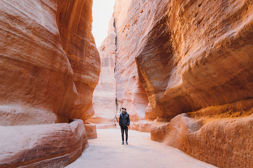 Young multiracial man explorer with backpack hiking in the beautiful pink canyon in the old town of Petra in the Middle East