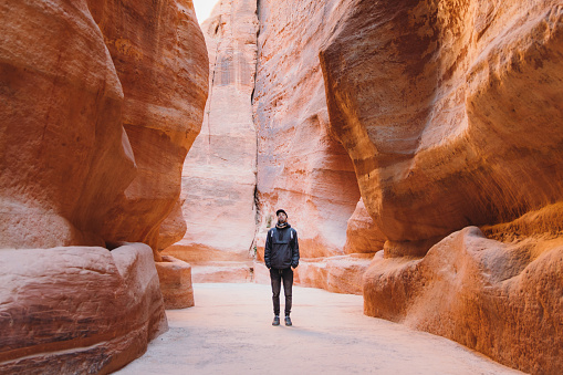 Young multiracial man explorer with backpack hiking in the beautiful pink canyon in the old town of Petra in the Middle East