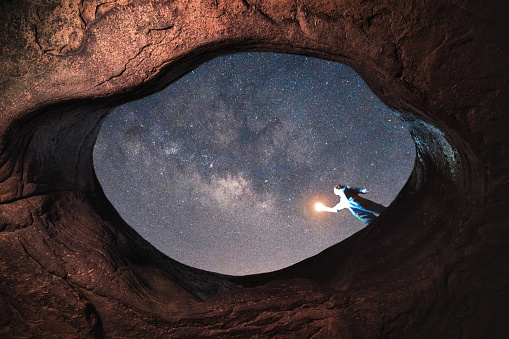 Woman holding lamp standing on top of big hole with milky way in the night sky at Sam Phan Bok