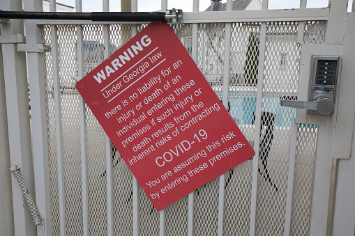 A covid-19 warning sign on a gate into a pool area.