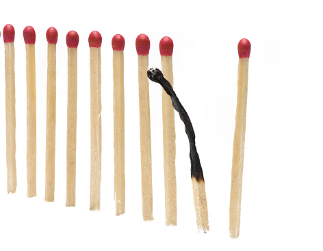 Close up of matches in an even row with a burned match behaving differently than concept for burnout on white background