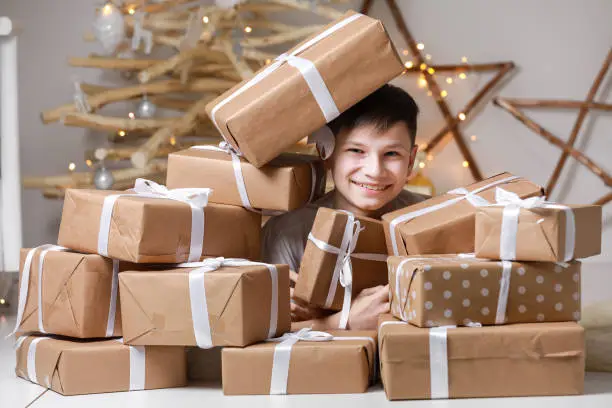 Photo of holiday shopping. child celebrating holidays near Christmas tree. smiling teenager boy is having fun with a lot of gift boxes. Happy new year. decorated Christmas tree.