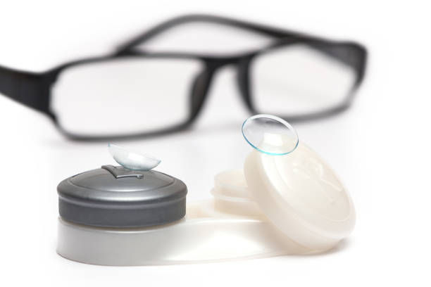 Contact lenses on lens case in front of black optical glasses on white background