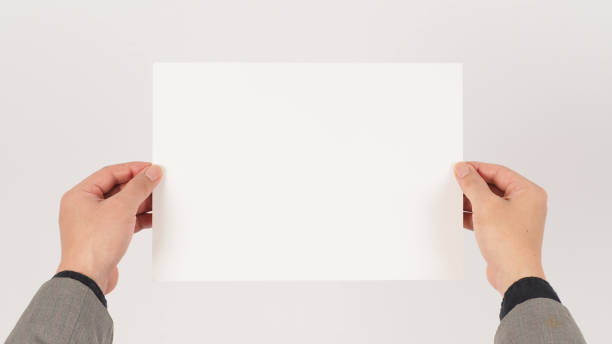 istock Space for text. The hand is wearing a gray suit and holding blank board A4 paper on white background. 1362934614