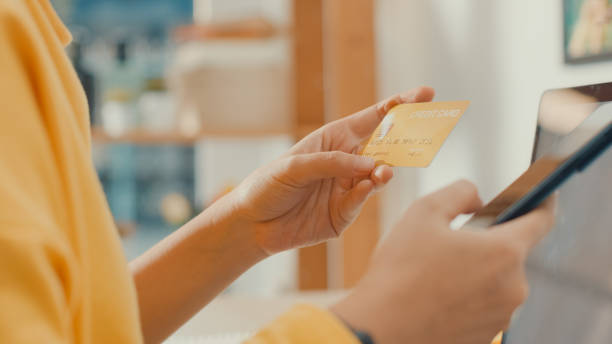 istock Young Asian woman using phone while performing online transactions with credit card during shopping in living room at home. 1362936259