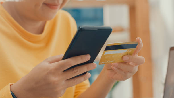 istock Young Asian woman using phone while performing online transactions with credit card during shopping in living room at home. 1362936323