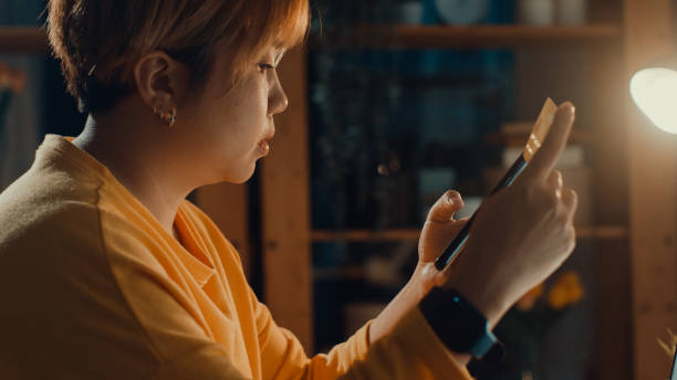 istock Young Asian woman using mobile phone while performing online transactions with credit card during shopping in living room at home at night. 1362936685