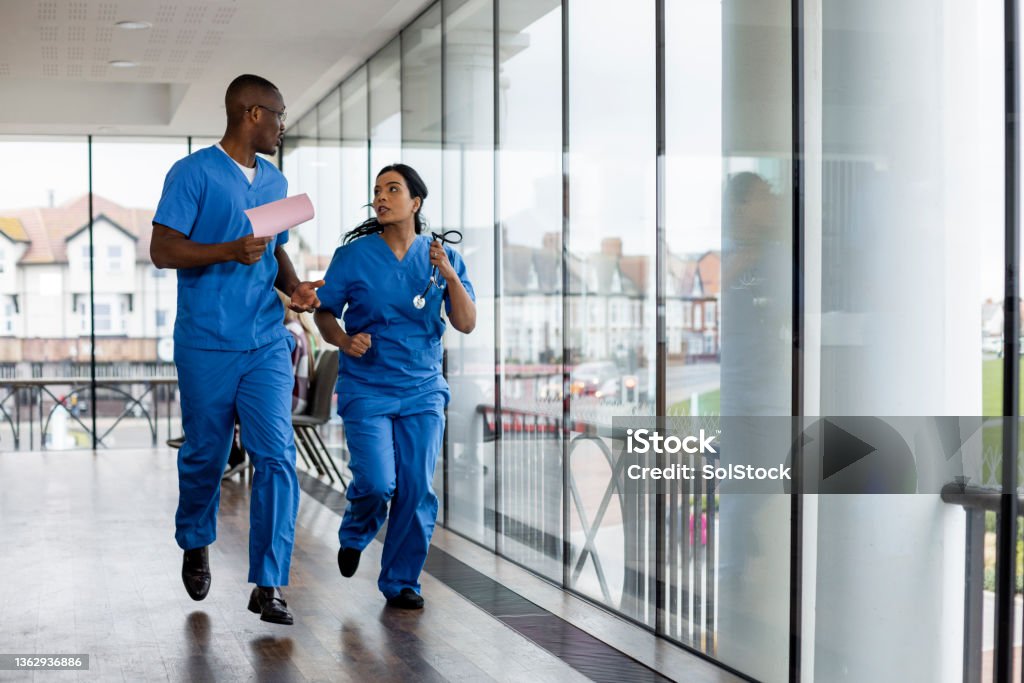 Doctors Running to Help Mixed ethnic group of medical professionals running down a corridor together in the North East of England. They are working a shift at a hospital and are dressed in scrubs. They are reacting to a medical emergency. Nurse Stock Photo