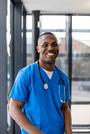 Medical professional working in a hospital in the North East of England. He is dressed in scrubs looking at the camera smiling with a stethoscope around his neck.