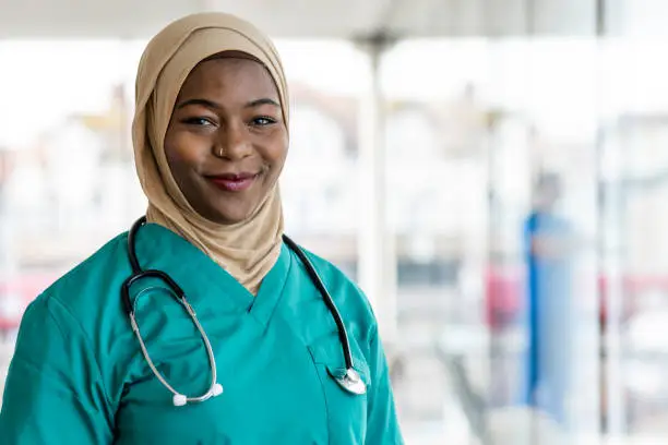 Portrait of a medical professional working in a hospital in the North East of England. She is dressed in scrubs with a stethoscope around her neck looking at the camera smiling.