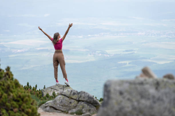 magnifique blonde aux cheveux longs en t-shirts roses et pantalons bruns se promène le long du chemin parmi les buissons de la montagne et profite de l’air frais et de la connexion avec l’énergie de la montagne, médite dans la position du lotus et s - hiking young women outdoors t shirt photos et images de collection