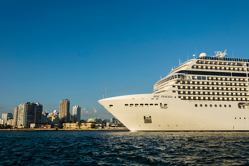 Santos, São Paulo - Brazil - December 20, 2014: Cruise ship MSC Poesia departing from the port of the city of Santos on a sunny day. In the background, Buildings on the city waterfront.