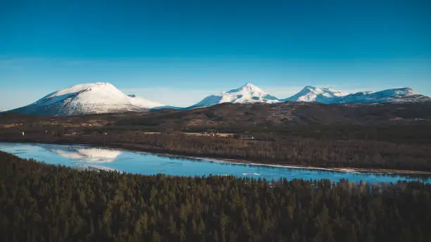 View of the wooded area and the Malselva River with a reflection on the snow-covered hills. Finnmark region, Nordland in northern Norway in beautiful sunny weather.