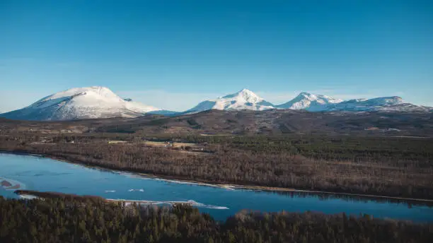 View of the wooded area and the Malselva River with a reflection on the snow-covered hills. Finnmark region, Nordland in northern Norway in beautiful sunny weather.