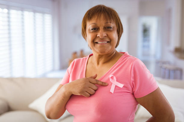 African american senior woman pointing at breast cancer awareness ribbon on pink t-shirt stock photo