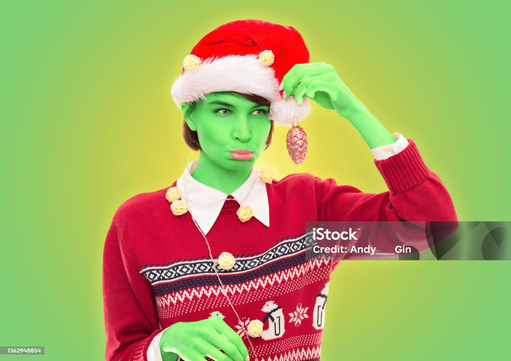 Image of a funny woman in a Christmas sweater posing on a white background with New Year's decorations. Grinch style. Holiday concept. Image of a funny woman in a Christmas sweater posing on a white background with New Year's decorations. Grinch style. Holiday concept. Mixed media Humor Stock Photo