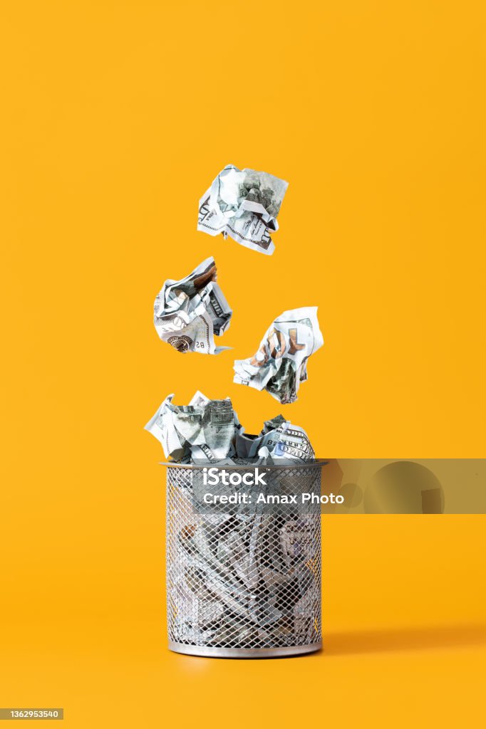 Concept of depreciation, waste of money. Dollar bills fall into the trash can on yellow background Currency Stock Photo
