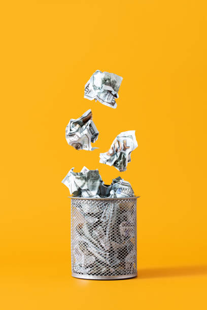Concept of depreciation, waste of money. Dollar bills fall into the trash can on yellow background stock photo