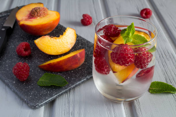 Detox or infused water with raspberry and peach in the drinking glass on the gray wooden background. Close-up. Detox or infused water with raspberry and peach in the drinking glass on the gray wooden background. Close-up. infused water stock pictures, royalty-free photos & images