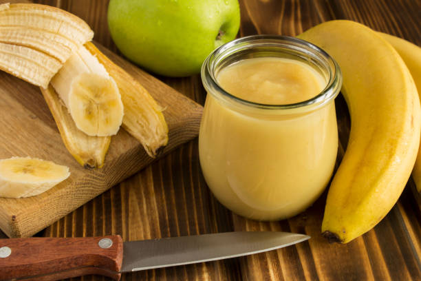 Puree with apple and banana in the small glass jar on the wooden background. Close-up. Puree with apple and banana in the small glass jar on the wooden background. Close-up. compote stock pictures, royalty-free photos & images