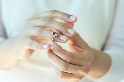 Hand of an unrecognizable female is about to wear a ruby ring.