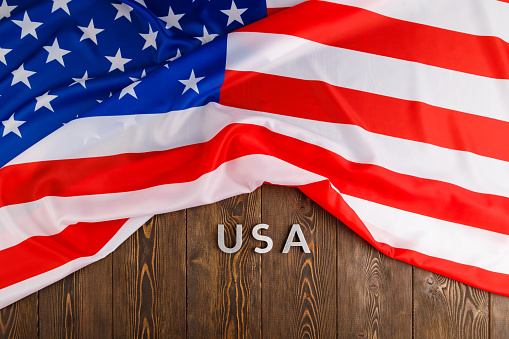 crumpled United States of America flag and with word USA laid with on flat textured wooden surface background in flat lay high angle view