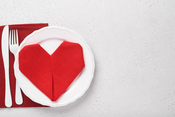 istock Valentinas day table setting white color with white silverware, red napkin folded as heart, candles, champagne, glasses on white background for greetings. Romantic dinner or menu concept. Mock up. 1362961246