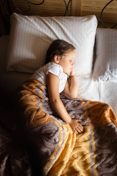 istock Young female kid sleeping and having rest on left side with one hand under head on big double bed covered with yellow gray blanket wearing home clothes 1362963897