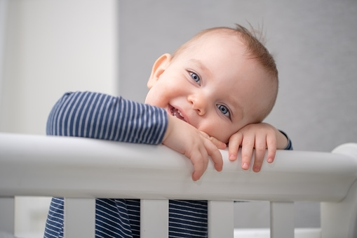 Portrait of a smiling boy holding the side of the crib and looking at the camera