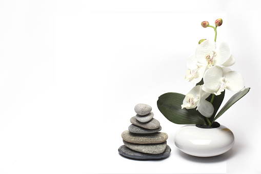 Close up of an artificial orchid next to stacked stones against white background as a concept for balance tranquility calming and wellness