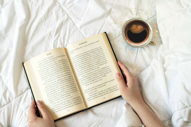 istock Woman's hands holding open book, girl reading book on the bed 1362968324