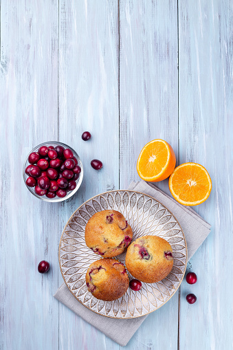 Homemade cranberry orange muffins on a wooden plate, vertical, top view, copy space