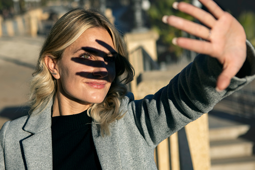 portrait of blonde woman facing the sun making shadow with her hand on her face revealing a green eye