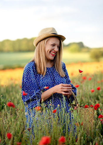 smiling woman in blue dress and hat walking in a field of flowers at sunset