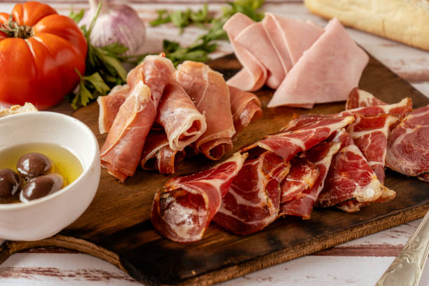 vista alta di un delizioso tavolo di prosciutto serrano, prosciutto cotto e mozzicone di maiale in salamoia accompagnato da olive nere. concetto di antipasto, - delicatessen meat cold cuts chopped foto e immagini stock