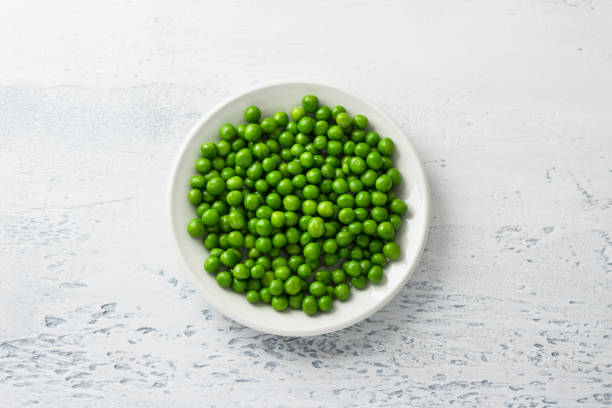 plato blanco con guisantes verdes al vapor sobre un fondo azul claro. ingrediente dietético saludable y delicioso para cocinar - guisante fotografías e imágenes de stock