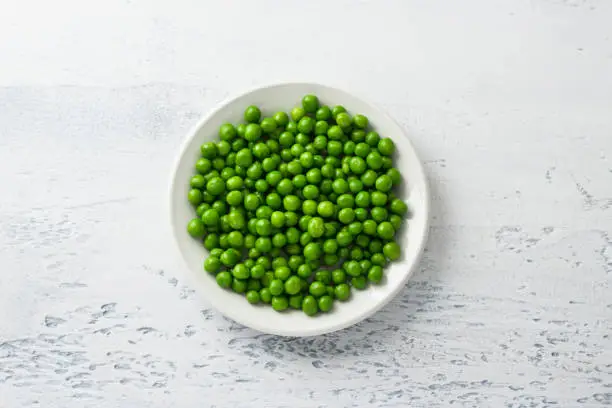 Photo of White plate with steamed green peas on a light blue background. Healthy delicious dietary ingredient for cooking