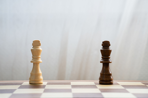 Black and white kings pieces apart on wooden chess board on light background. Interracial relationships and multi-ethnic diversity support concept