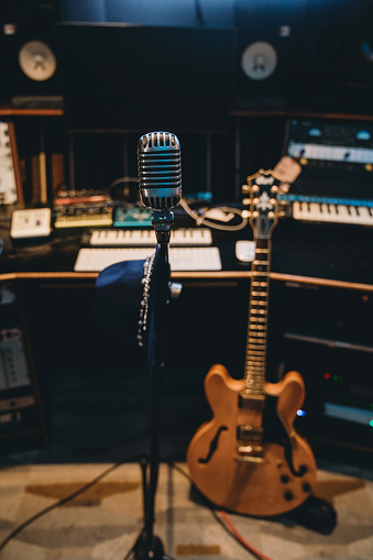 A vintage microphone in a professional recording studio. A guitar is on the backgraound.