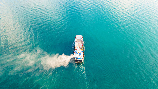 Aerial view of a container ship carrying cargo for an import-export logistics business in the sea. Smoke from a ship sailing in the sea - A picture from a drone of a ship carrying a cargo on the ocean. There is white smoke coming from the ship. Fishing vessel sailing on the sea. Sea photo. A boat sailing on the high seas.