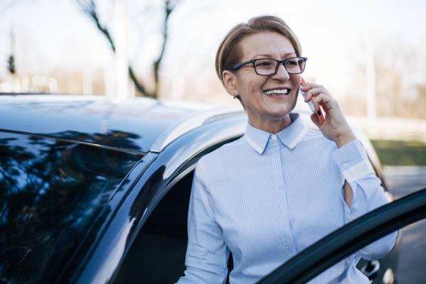車のそばに立っている成熟した女性。 - car smart phone business businesswoman ストックフォトと画像