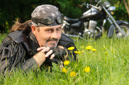 The picture of a biker lying on grass, looking at dandelions and smiling