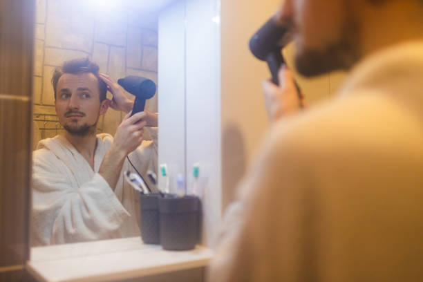 jeune homme en peignoir se séchant les cheveux après une douche dans un miroir de salle de bain brumeux - toothbrush brushing teeth brushing dental hygiene photos et images de collection