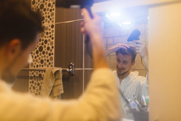 jeune homme en peignoir se séchant les cheveux après une douche dans un miroir de salle de bain brumeux - toothbrush brushing teeth brushing dental hygiene photos et images de collection