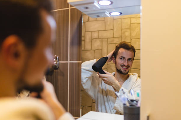 istock Smiling young man in a bathrobe blow drying his hair after taking a shower while looking at himself in the bathroom mirror 1362982639