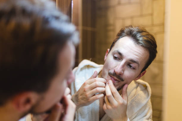 istock Young man in a bathrobe popping pimples while looking at himself in the mirror after a shower 1362982664