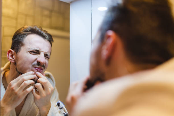 istock Young man in a bathrobe popping pimples while looking at himself in the mirror after a shower 1362982667