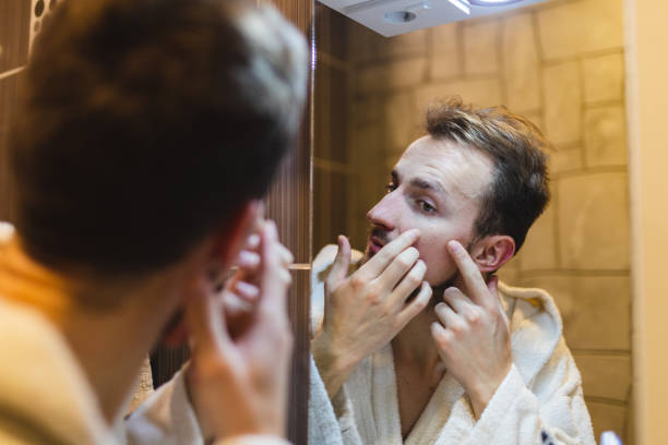 jeune homme en peignoir faisant éclater des boutons tout en se regardant dans le miroir après une douche - toothbrush brushing teeth brushing dental hygiene photos et images de collection