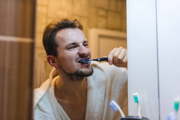 istock Young man wearing a bathrobe brushing his teeth while looking at himself in the bathroom mirror 1362982696