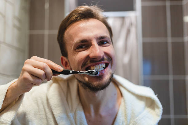 gros plan d’un jeune homme portant un peignoir et se brossant les dents dans la salle de bain - brushing teeth photos et images de collection